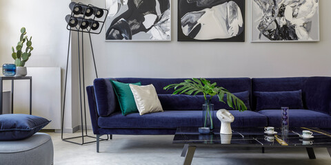 Stylish and modern living room interior with blue velvet sofa, mock up paintings, design furniture,...