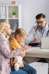 Mother looking at diseased kid near pediatrician on blurred background