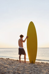 Surfer standing with surfboard on sandy sea beach