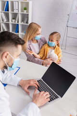 Fototapeta premium Child in medical mask talking near mother and family doctor using laptop
