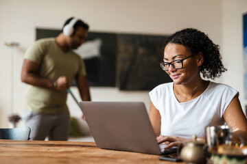 Obraz premium Woman with vitiligo working with laptop while his boyfriend cleaning floor