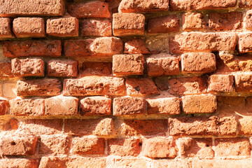 Obraz premium Fragment of a brick ruin wall. The red brick has partially collapsed over time and under the influence of weather. The surface has numerous depressions. Background. Texture.