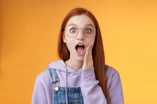Omg no way. Attractive shocked wondered redhead amused hipster woman modern teenager drop jaw gasping wide eyes surprised standing amazed reacting shocked camera touch cheek excited