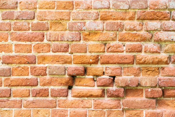 Old wall of red bricks of various shades. Several bricks have crumbled from the impact of time and natural conditions. Background. Texture.