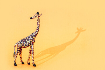 Fototapeta premium Wooden Giraffe Figurine with shadow on orange background with copy space