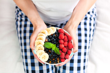 Female hands hold a bowl of granola with fresh berries and banana. Healthy breakfast. Сlose-up. Top view.