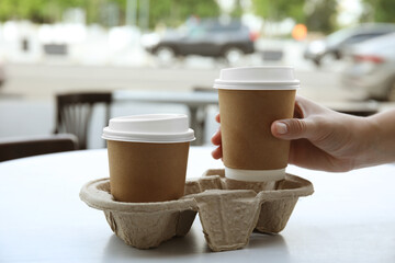 Woman taking paper coffee cup from cardboard holder at table outdoors, closeup