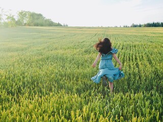 Happy woman in dress running in sunlight on summer field, enjoying life. Girl brunette long black hair fly in wind. Nature beauty, blue sky, field wheat. Freedom, Sustainable lifestyle, Wellness