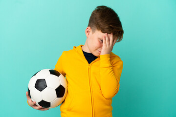 Redhead kid playing football isolated on blue background with tired and sick expression