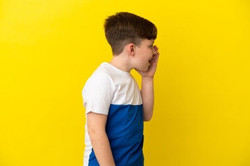 Little redhead boy isolated on yellow background shouting with mouth wide open to the side