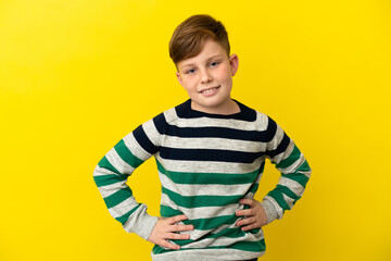 Little redhead boy isolated on yellow background posing with arms at hip and smiling