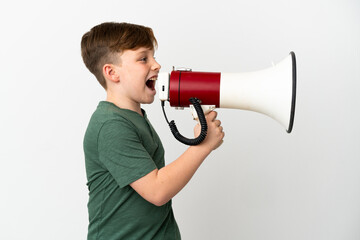 Naklejka premium Little redhead boy isolated on white background shouting through a megaphone to announce something in lateral position