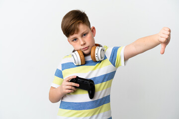 Little redhead boy holding a game pad isolated on white background showing thumb down with negative expression