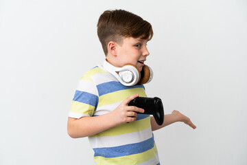 Little redhead boy holding a game pad isolated on white background with surprise expression while looking side