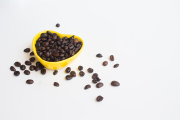 Fototapeta na wymiar A dark brown coffee beans in small yellow heart bowl on white background