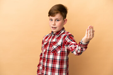 Little redhead boy isolated on beige background inviting to come with hand. Happy that you came