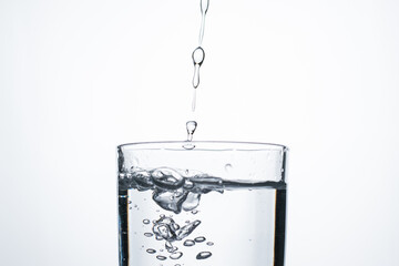 Jet of water or alcohol is pouring into a glass with splashes and bubbles, copy space