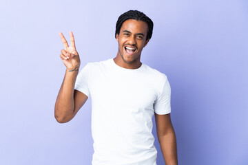 Fototapeta premium Young African American man with braids man isolated on purple background smiling and showing victory sign