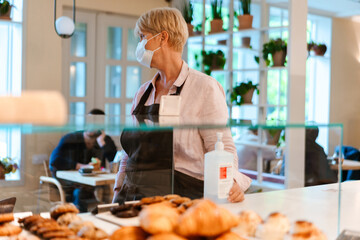 Mature woman wearing face mask using sanitizer while working in cafe