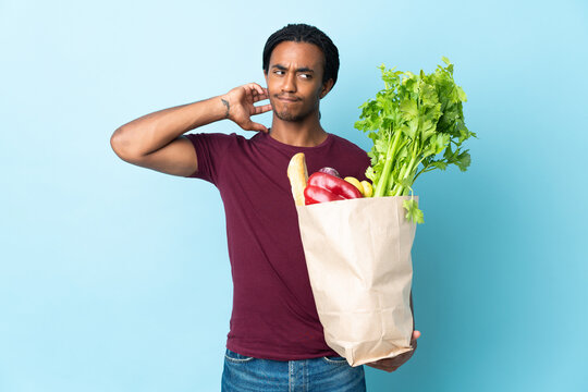 African American Man Holding A Grocery Shopping Bag Isolated On Blue Background Having Doubts