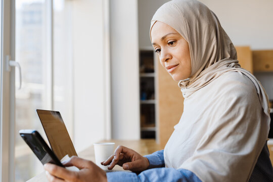 Middle eastern woman in hijab working with laptop and smartphone