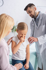 Fototapeta premium Kid sneezing near mother and doctor with stethoscope