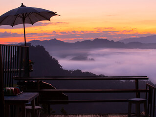 The sillouette umbrella on wooden terrace on the mountain covered by sea of fog on the morning and have twilight ray on sky before sunrise.
