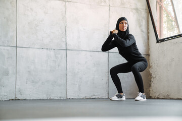 Young muslim woman in hijab doing exercise while working out indoors
