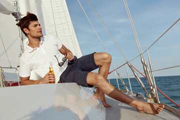 Young man drinking beer on his yacht in sea