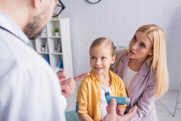 woman looking at family doctor pointing at inhaler near smiling daughter