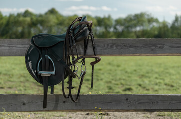 Saddle and bridle are on a wooden fence in outdoors.