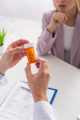 cropped view of physician holding container with pills near blurred patient