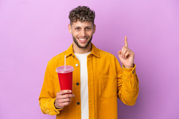 Young blonde man holding soda isolated on purple background pointing up a great idea