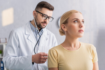 doctor in eyeglasses examining blonde woman with stethoscope