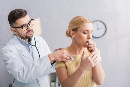 sick woman coughing near doctor examining her with stethoscope in clinic