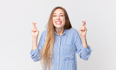 pretty thin woman smiling and anxiously crossing both fingers, feeling worried and wishing or...