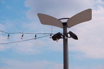 Modern park lighting pole with LED spotlights and reflectors against a blue sky.