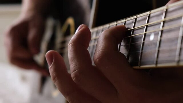 Playing the guitar. Strumming acoustic guitar. Musician plays music. Man fingers holding mediator. Man hand playing guitar neck in dark room. Unrecognizable person rehearsing, fretboard close-up.