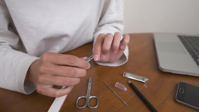 Close-up of a young caucasian woman doing a manicure by cutting off nails and cuticles at home.