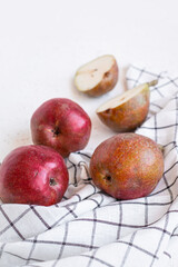 Ripe organic red pears and slices of pears on white checkered dishcloth on white stone background. Fresh pear closeup.