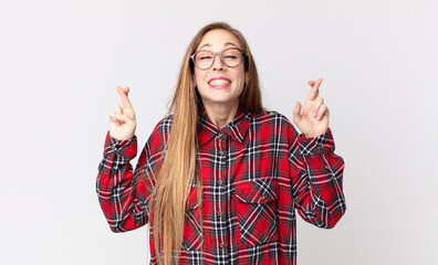 pretty thin woman smiling and anxiously crossing both fingers, feeling worried and wishing or...