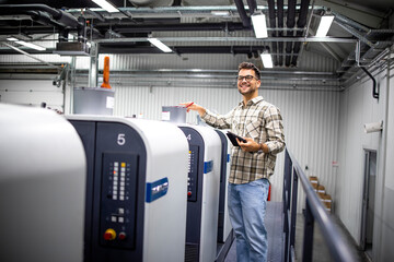 Portrait of professional graphic designer or engineer checking production on offset printing machine in print factory.