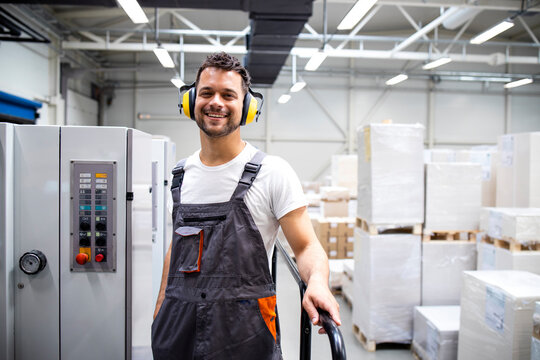 Portrait of an experienced print worker standing by modern printing machine with large piles of sheets in background.