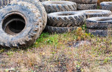 Fototapeta na wymiar Used old truck tires on grass. Old worn-out tyre are valuable raw material for enterprises based on recycling of waste, for their reuse for manufacture of industrial rubber products. Selective focus.