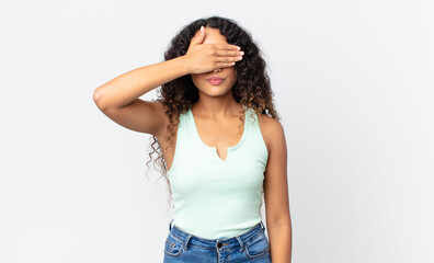 pretty hispanic woman covering eyes with one hand feeling scared or anxious, wondering or blindly...