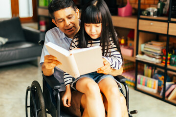 Senior asian male smiling and reading interesting fairytale to curious girl while sitting on sofa and resting together.