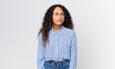 pretty hispanic woman looking puzzled and confused, wondering or trying to solve a problem or...