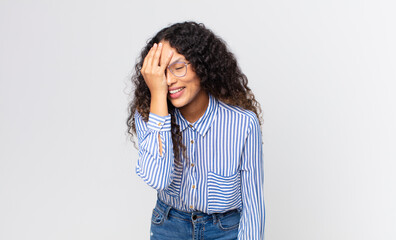 pretty hispanic woman laughing and slapping forehead like saying d’oh! I forgot or that was a...
