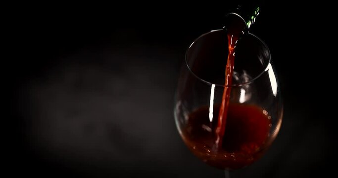 red wine pouring into a glass from bottle on a black background. copy space