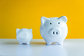 Two white piggy bank on the table and yellow background save money concept.